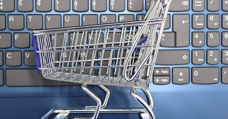 A miniature shopping cart placed on a laptop keyboard symbolizing online shopping and e-commerce.